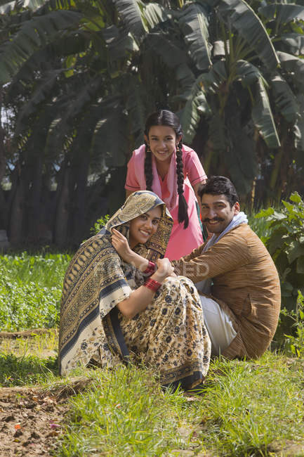 Sonriente familia india sentada en el campo agrícola - foto de stock