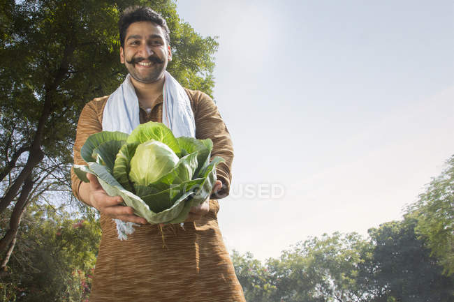Vista basso angolo di contadino indiano sorridente che tiene grande cavolfiore — Foto stock