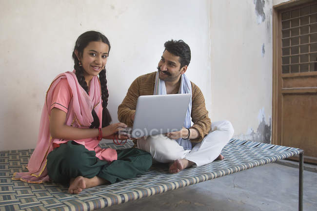 Дівчина сидить з батьком на ліжку і використовує ноутбук — стокове фото
