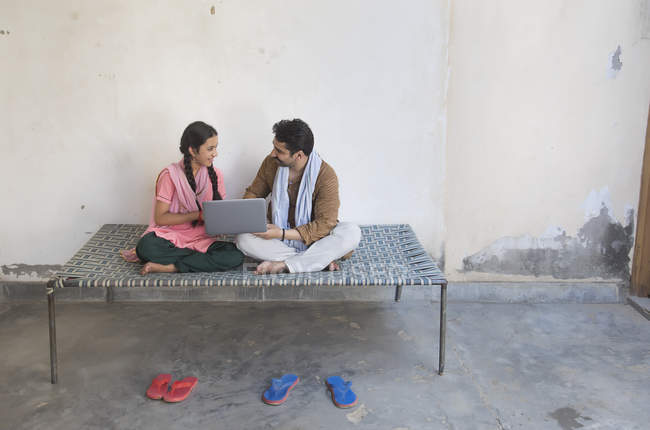 Девушка сидит с отцом на детской кроватке и с помощью ноутбука — стоковое фото