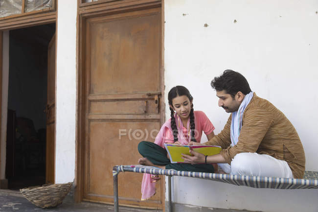 Девушка сидит с отцом на детской кроватке и читает книгу — стоковое фото