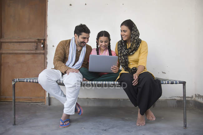 Indisches Mädchen sitzt mit Eltern auf Kinderbett und benutzt Laptop-Computer — Stockfoto