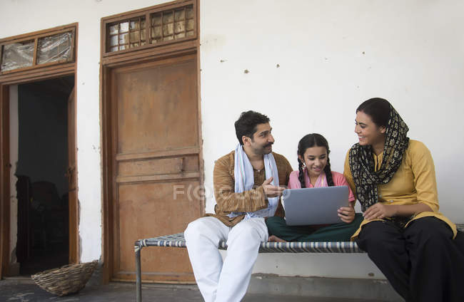 Индийская девушка сидит с родителями на детской кроватке и с помощью ноутбука — стоковое фото