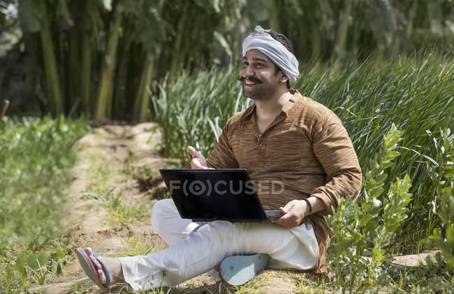 Indian farmer using laptop using computer in agriculture field — Stock Photo