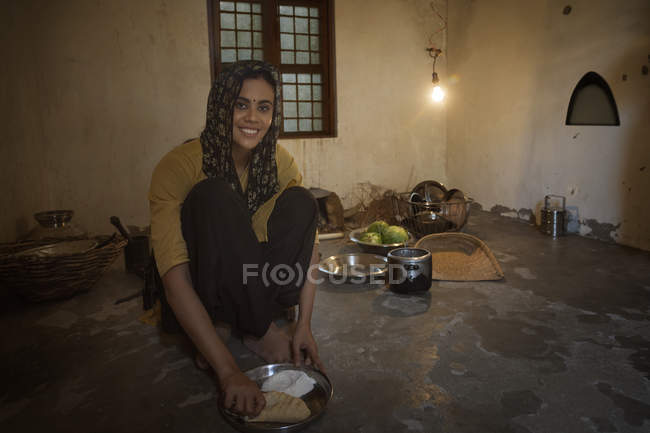 Femme indienne assise dans la cuisine et cuisiner des aliments sur du bois de chauffage avec des ustensiles — Photo de stock