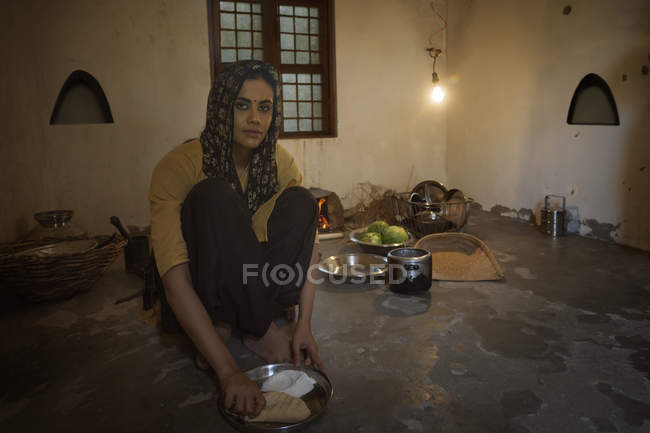 Индийская женщина сидит на кухне и готовит еду на дровах с посудой — стоковое фото