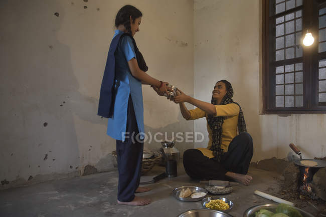 Indian woman cooking food and giving tiffin box to daughter — Stock Photo