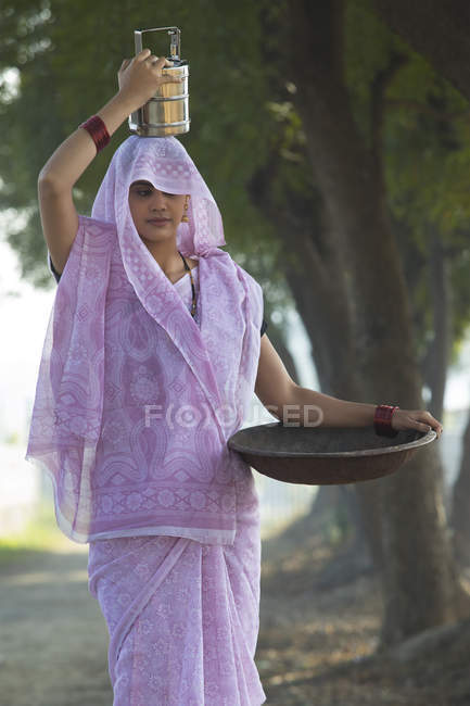 Mulher indiana carregando caixa de tiffin na cabeça e ferro panela de ouro na mão — Fotografia de Stock