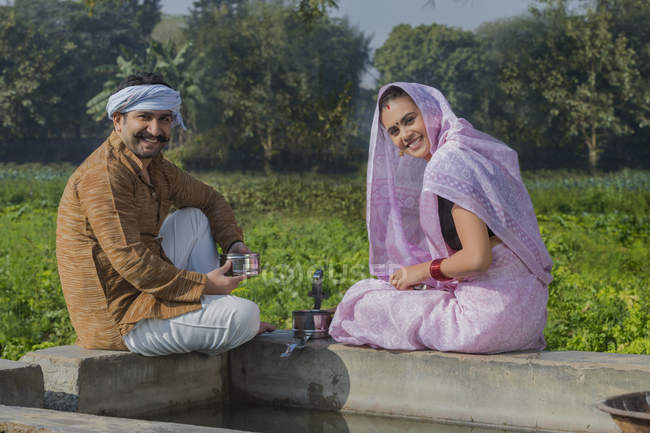 Casal indiano sentado perto de tanque de água no campo agrícola — Fotografia de Stock