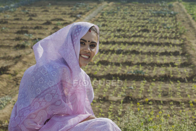 Портрет улыбающейся сельской женщины, покрывающей голову сари, сидящей на поле — стоковое фото