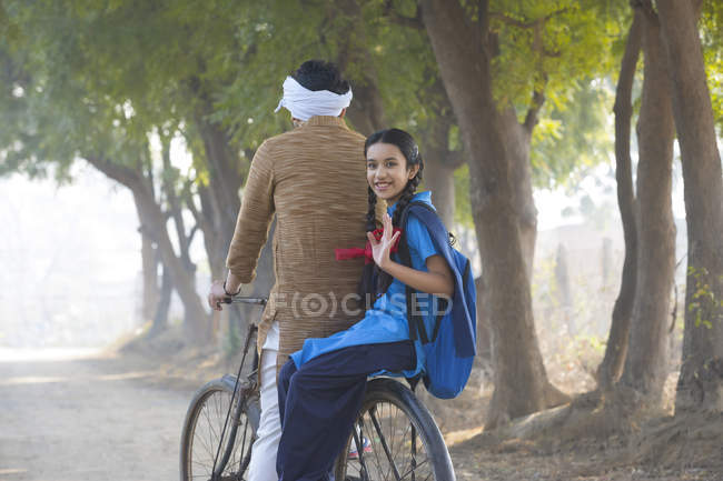 Vista posteriore di scolaretta felice in bicicletta con padre nel villaggio — Foto stock