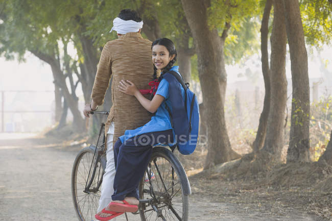 Rear view of happy schoolgirl riding on bicycle with father in village — Stock Photo