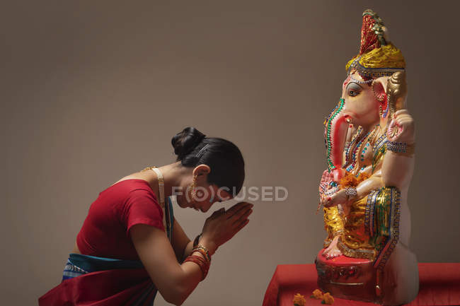 Mujer rezando con las manos unidas y los ojos cerrados delante de Ganpati ídolo - foto de stock