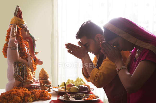 Муж и жена молятся с поднятыми руками перед идолом Ганеша — стоковое фото