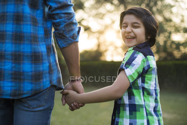 Vista posteriore del ragazzo felice che tiene la mano del padre nel parco — Foto stock