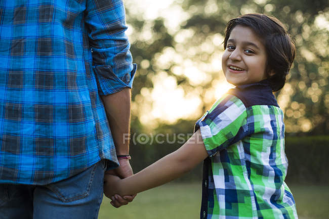 Вид сзади счастливого мальчика, держащегося за руку отца в парке — стоковое фото