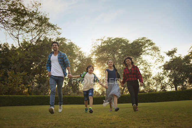 Familia india feliz cogida de la mano al caminar en el parque - foto de stock
