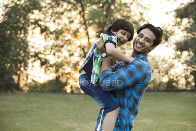 Усміхнений індійський чоловік грає з дитиною в парку — стокове фото