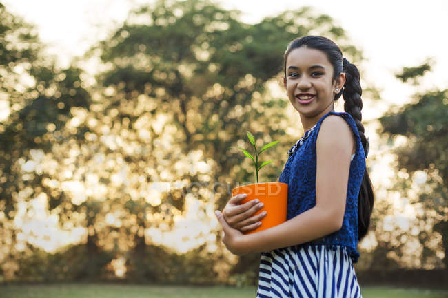 Vista a basso angolo di sorridente ragazza che tiene il vaso di fiori in mano al parco — Foto stock