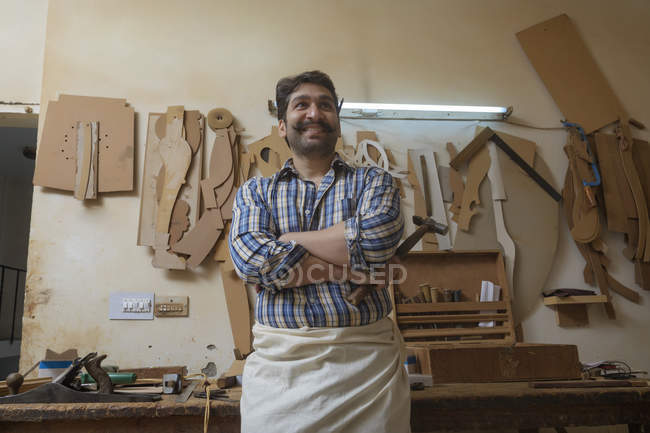 Portrait de menuisier debout dans son atelier tenant un marteau avec les bras croisés — Photo de stock