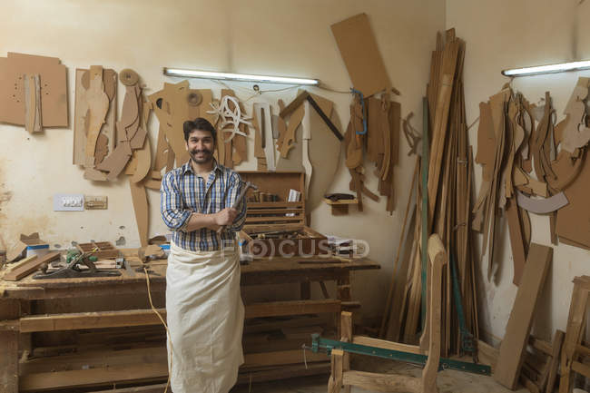 Retrato de carpinteiro em pé em sua oficina segurando um martelo com os braços cruzados — Fotografia de Stock