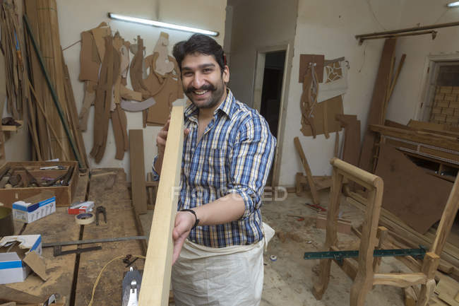 Lächelnder Tischler in der Werkstatt überprüft Geradlinigkeit von Holzstämmen — Stockfoto