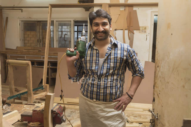 Улыбающийся плотник позирует с буровой машиной в мастерской — стоковое фото