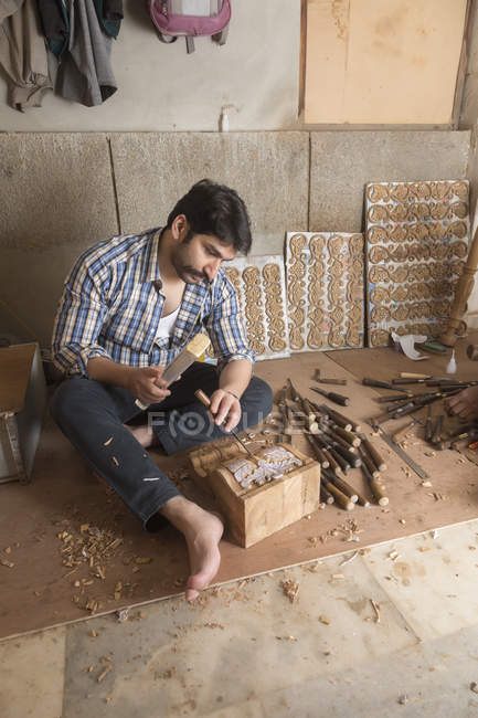 Carpenter making carvings and designs on wood using chisel in workshop — Stock Photo