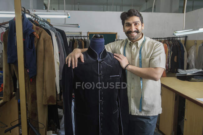 Tailleur debout à côté du mannequin portant un manteau semi-cousu en atelier — Photo de stock