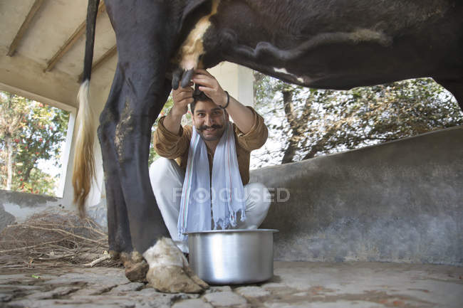 Visão de baixo ângulo de leiteiro sorridente vaca ordenha — Fotografia de Stock