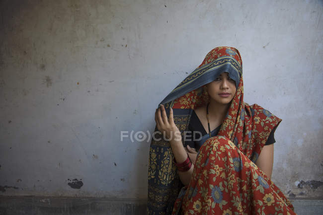 Smiling woman sitting on floor and covering head with sari — Stock Photo