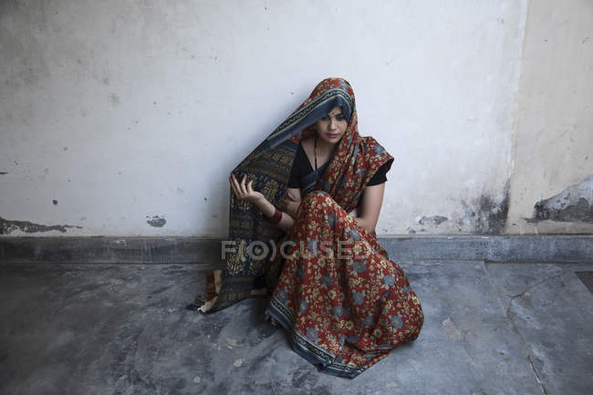 Vista de ángulo alto de la mujer sentada en el suelo y cubriendo la cabeza con sari - foto de stock