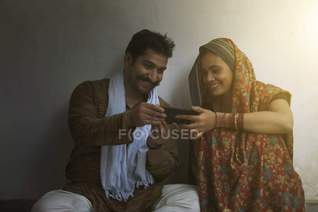 Sonriente pareja sentada en el suelo y usando el teléfono móvil - foto de stock