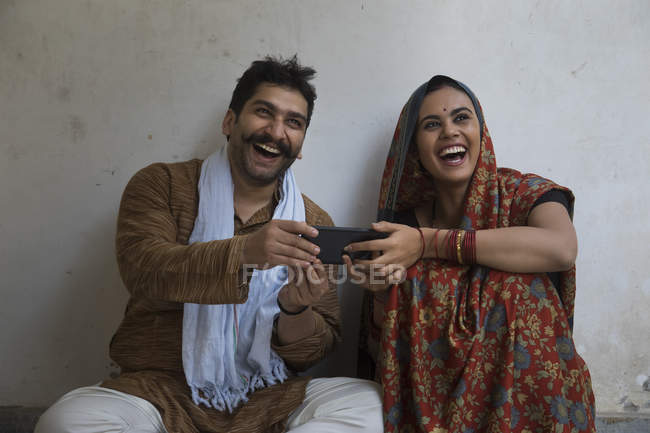 Lächelndes Paar sitzt auf dem Boden und benutzt Handy — Stockfoto