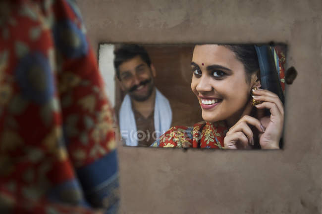 Smiling woman looking in mirror and wearing ear rings with — Stock Photo