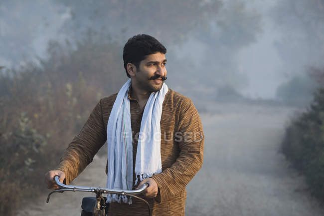 Мужчина фермер на сельской дороге держит велосипед и смотрит в сторону туманного утра — стоковое фото