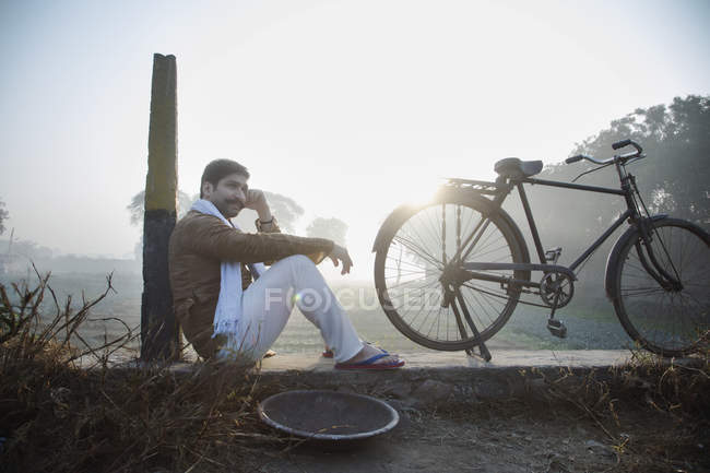 Farmer sitting near agriculture field with bicycle and talking at mobile phone — Stock Photo