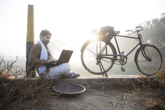 Landwirt sitzt in der Nähe von Ackerland und benutzt Laptop-Computer — Stockfoto