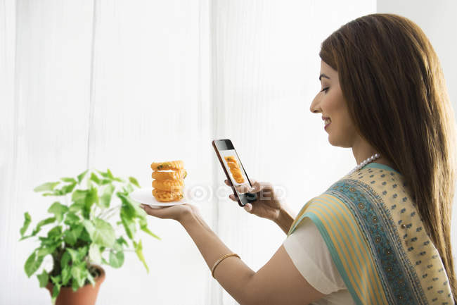 Mujer haciendo clic foto de plato dulce en la mano - foto de stock