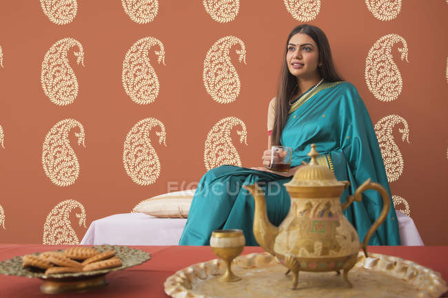 Mujer en saree tomando té en casa - foto de stock