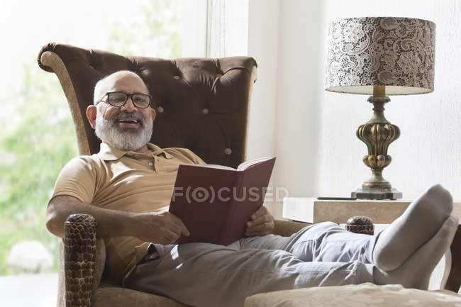 Alter Mann lacht, während er ein Buch liest — Stockfoto