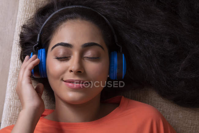 Schöne Frau, die Musik hört, während sie auf der Couch liegt — Stockfoto