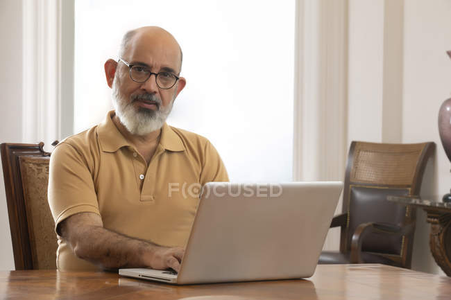 Старик сидит за обеденным столом со своим ноутбуком. (Senior ) — стоковое фото