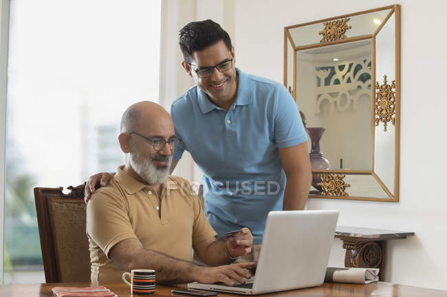 Père et fils regardant l'ordinateur portable tout en effectuant un paiement en ligne. (Famille ) — Photo de stock