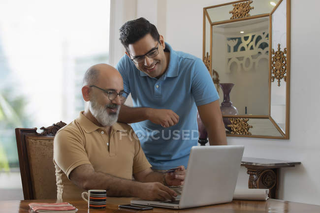 Padre e hijo mirando el portátil mientras hacen un pago en línea. (Familia) ) - foto de stock