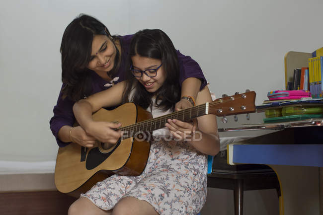 Mother helps her daughter play the guitar — Stock Photo