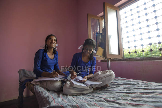 Two school girls laughing while studying at home — Stock Photo