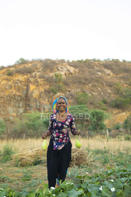 Donna in possesso di bottiglia zucca e sorridente, nel campo — Foto stock