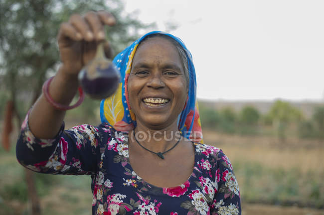 Donna che tiene brinjal e sorridente, nel campo — Foto stock