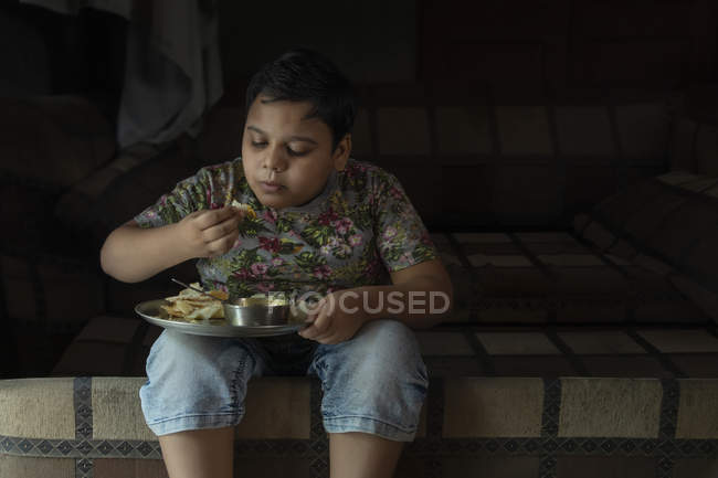 Jeune garçon assis sur le lit et ayant à manger — Photo de stock